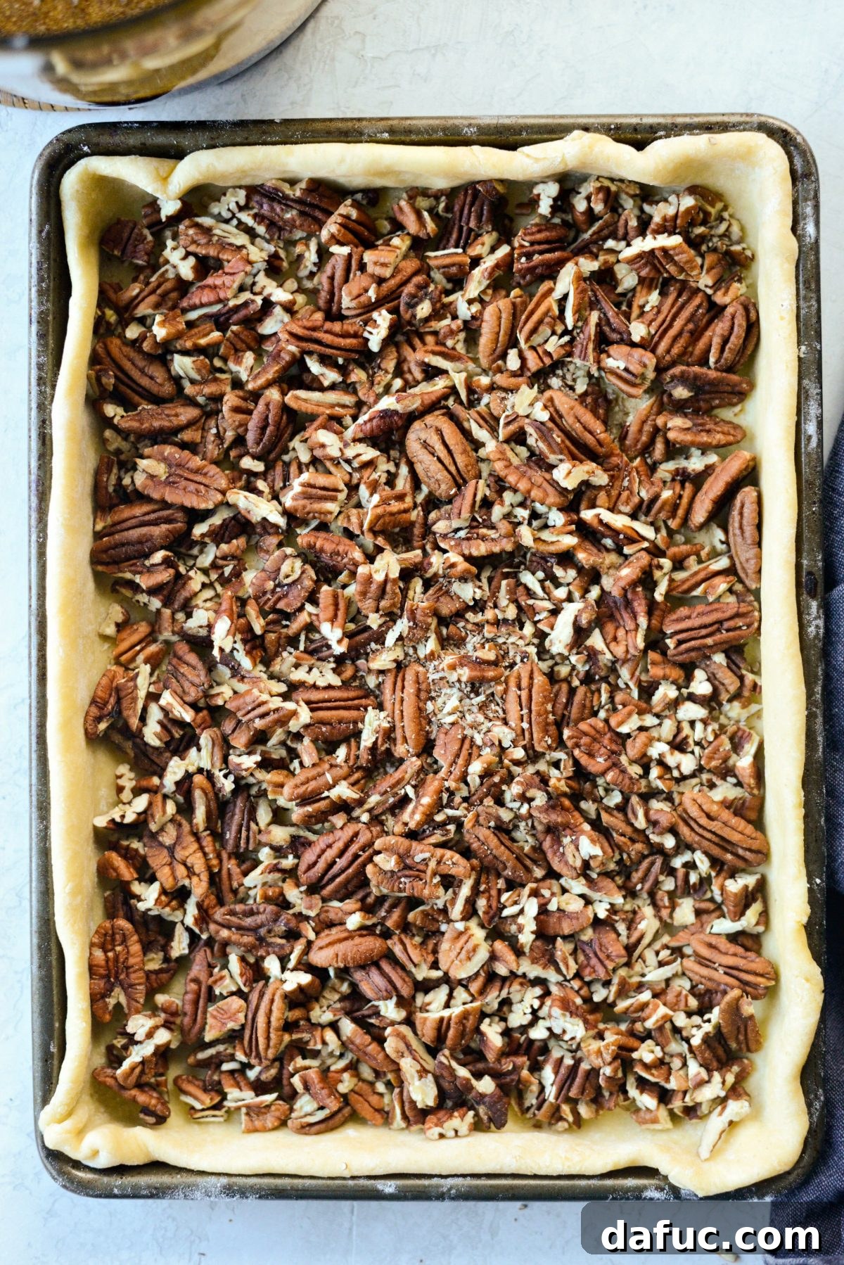 Adding coarsely chopped pecans to the unbaked pie crust in a sheet pan
