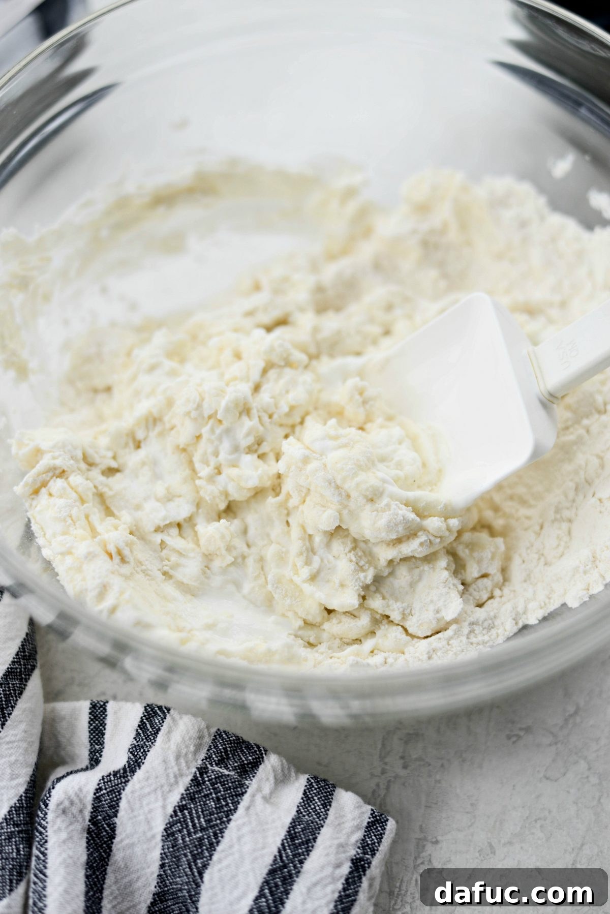 Stirring Greek yogurt and dry ingredients with a rubber spatula to form a shaggy dough