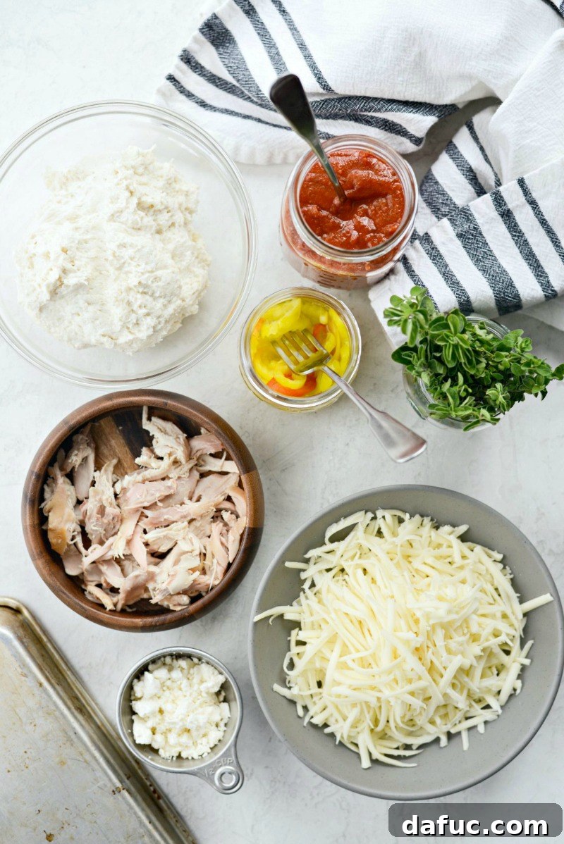 Spicy Chicken Feta Pizza ingredients laid out on a kitchen counter, including dough, sauce, cheese, chicken, peppers, and feta