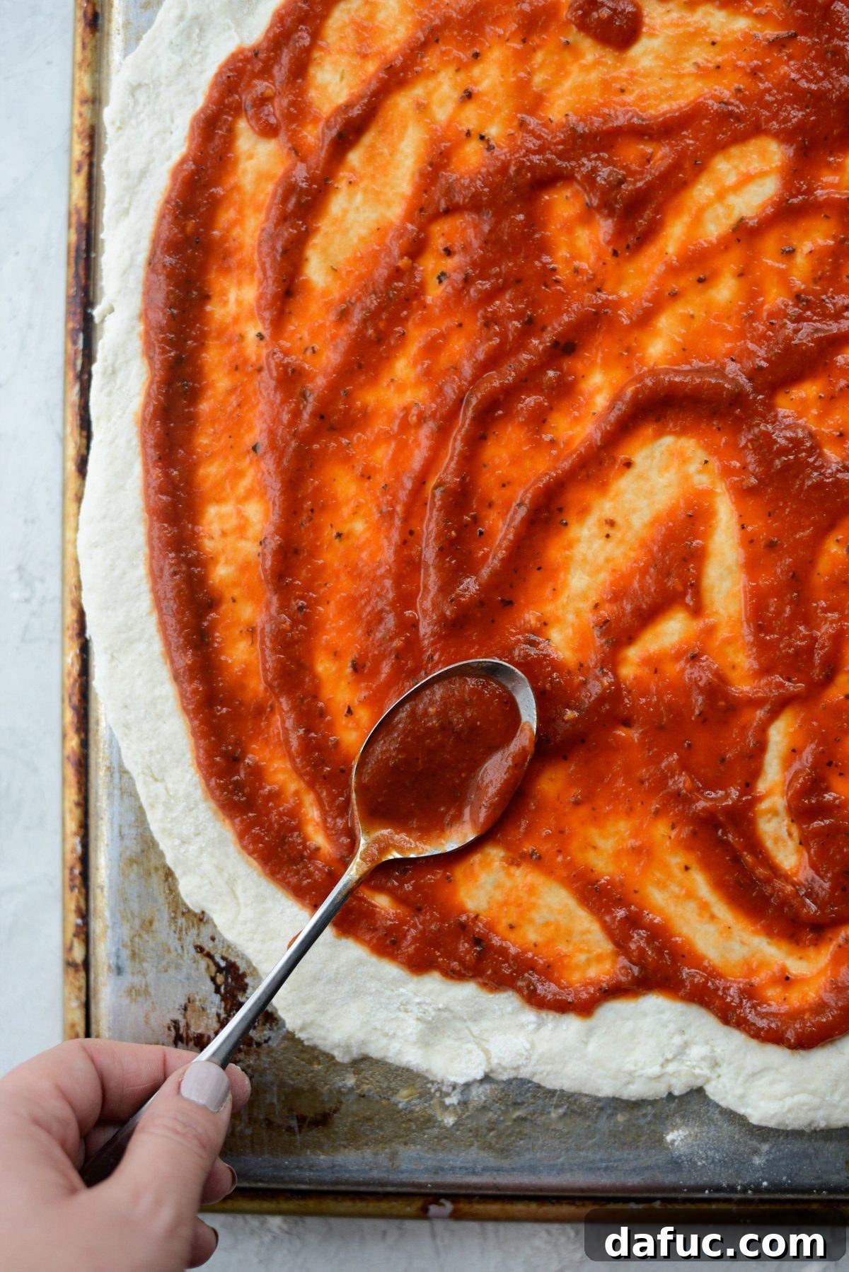 Spreading pizza sauce evenly on the rolled out Greek yogurt pizza dough, leaving a crust edge