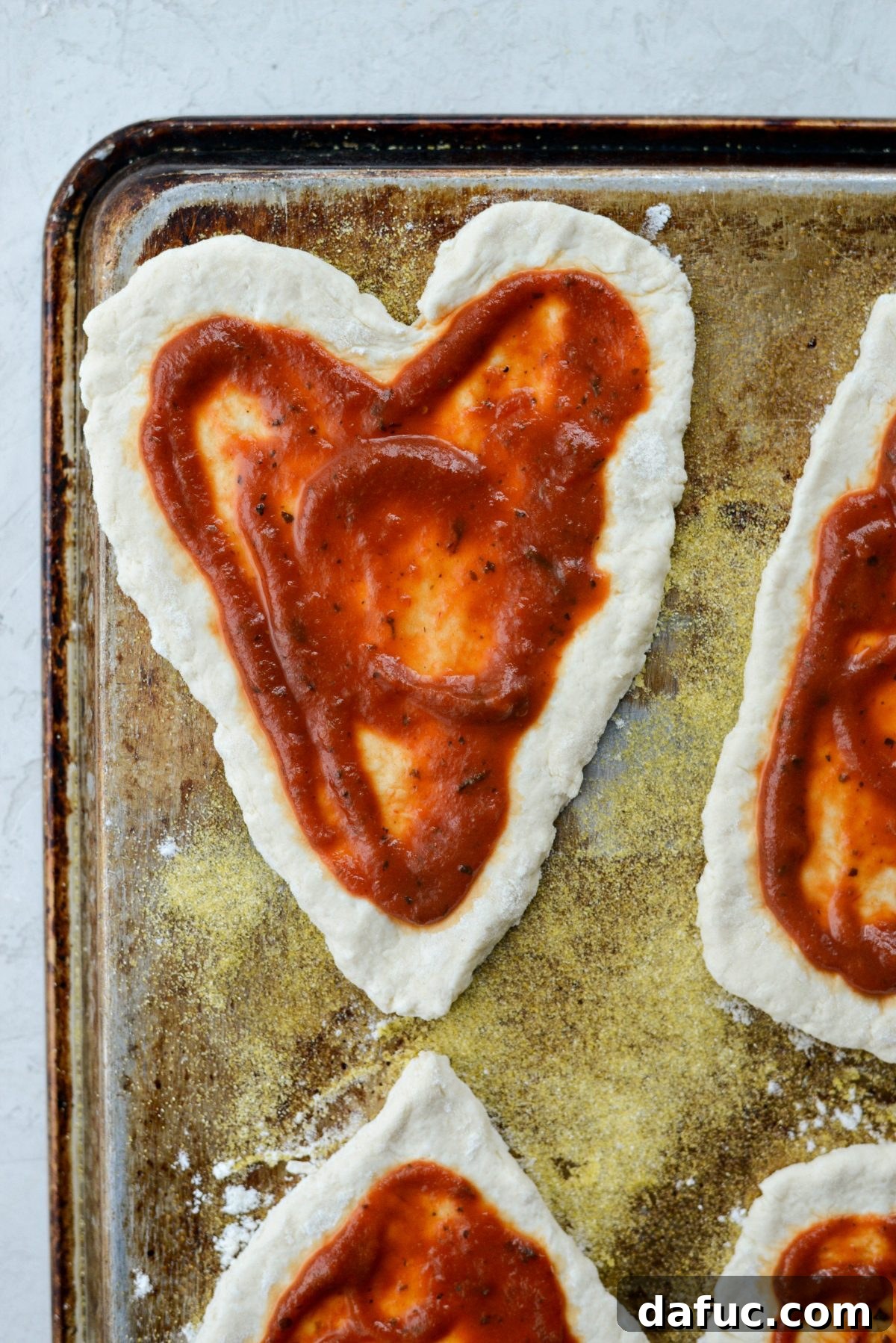 Sweetheart Pizza Treats 11 Pizza sauce spread on heart shaped pizza dough, leaving a crust edge