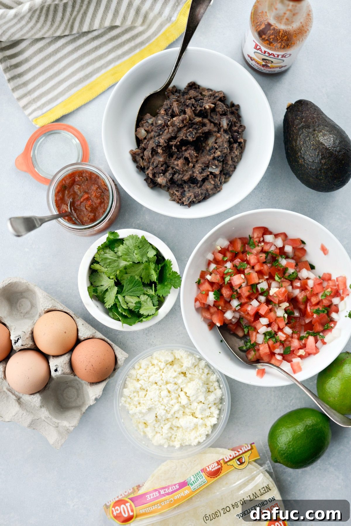 A collection of fresh ingredients for Huevos Rancheros, including eggs, tortillas, avocado, and pico de gallo components