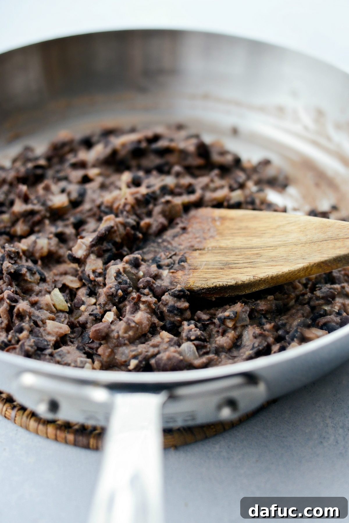Refried black beans being prepared in a skillet with onions and spices