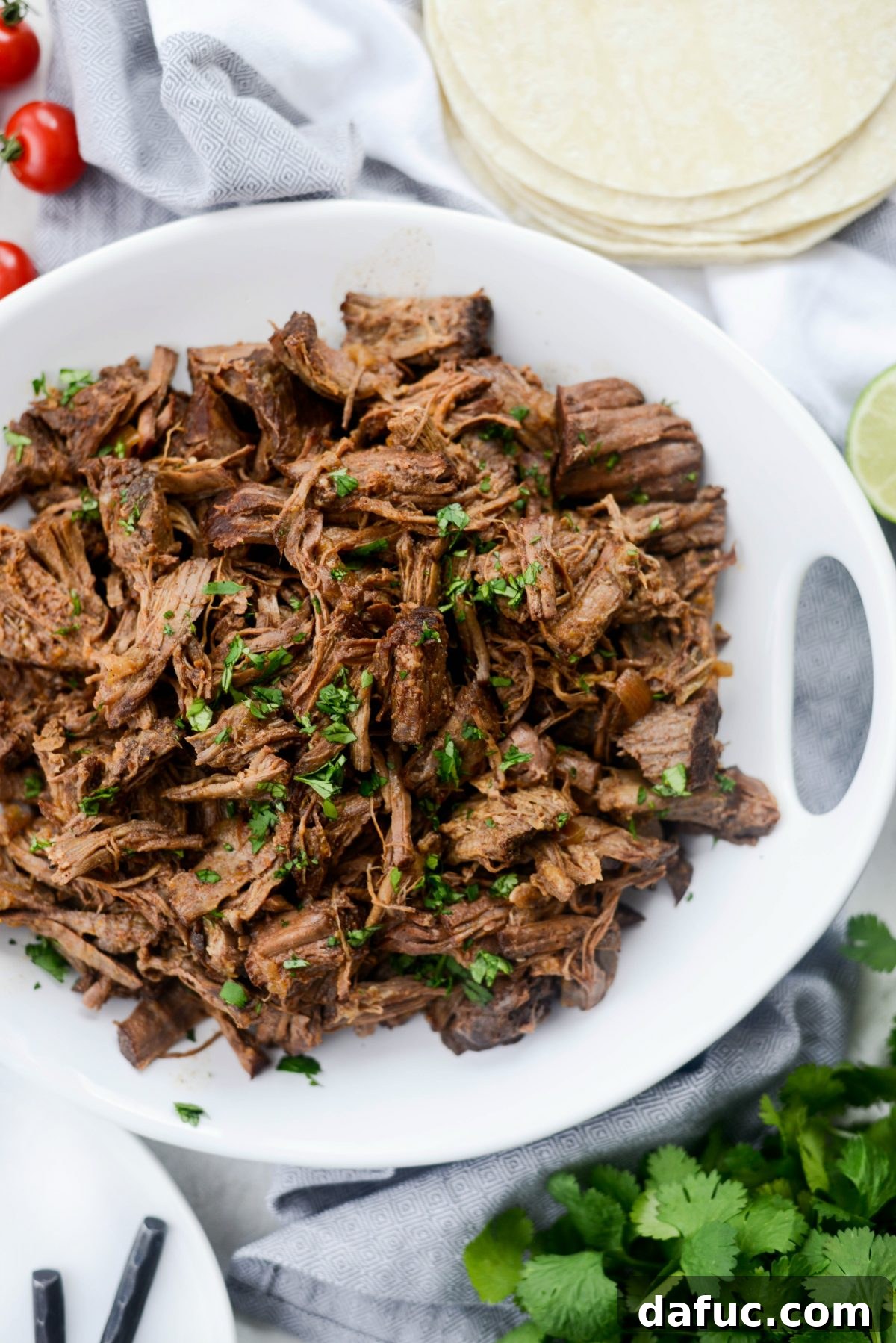 Fall-Apart Tender Slow Cooker Beef Barbacoa 2 A large serving platter filled with Slow Cooker Beef Barbacoa, garnished with fresh cilantro and lime wedges, ready to be enjoyed.