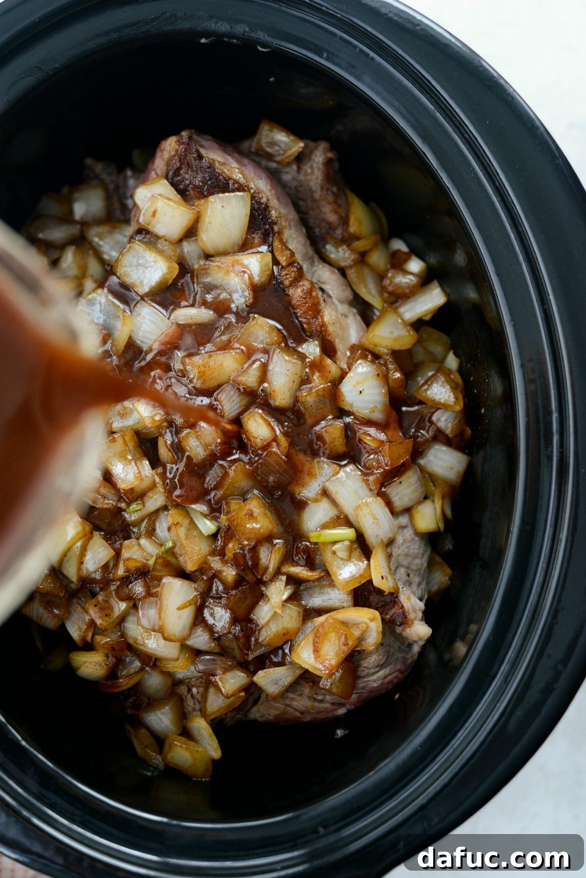 Fall-Apart Tender Slow Cooker Beef Barbacoa 11 The rich cooking liquids being poured over the beef and onions in the slow cooker, creating a flavorful broth.