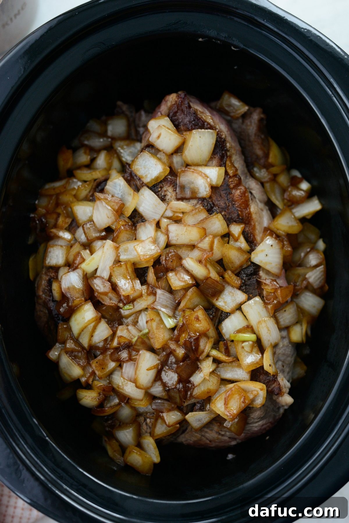 Fall-Apart Tender Slow Cooker Beef Barbacoa 10 Sautéed onions being added to the seared beef and other ingredients already in the slow cooker.