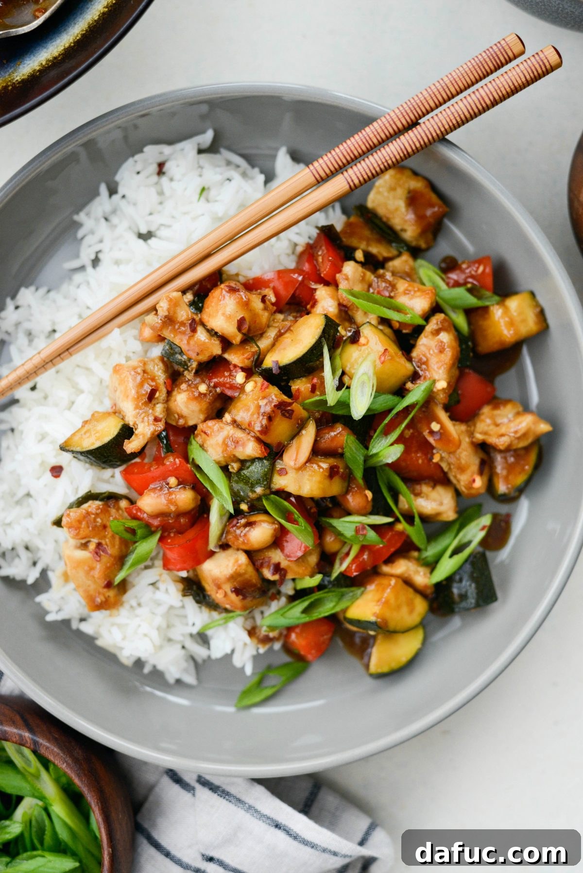 Authentic Homemade Kung Pao Chicken Stir-fry in a grey bowl, garnished with green onions and ready to serve with chopsticks.