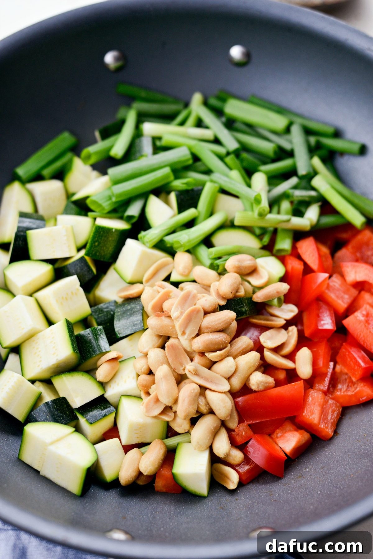 Fresh zucchini, red bell pepper, green onions, and peanuts added to a hot wok, ready for stir-frying.
