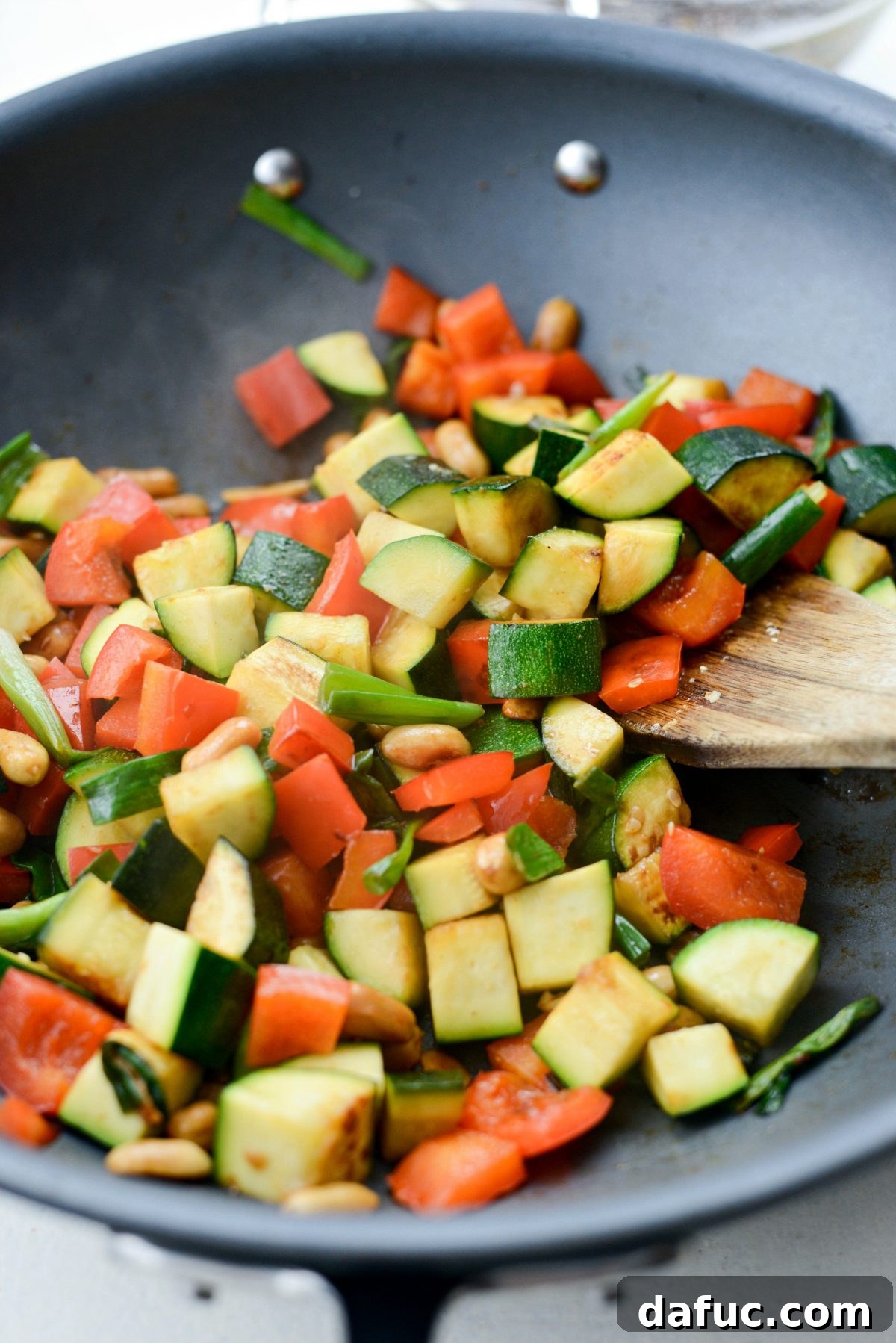 Vibrant vegetables, including zucchini, red bell pepper, and green onions, sautéing in a wok.