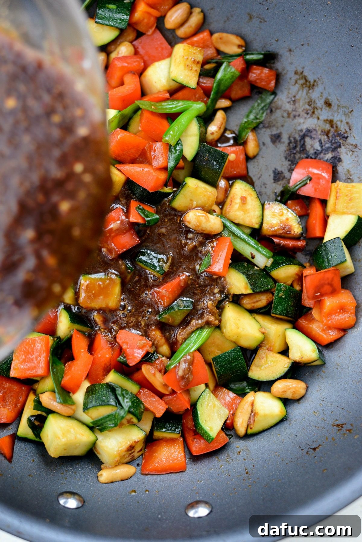 The rich Kung Pao sauce being poured into the wok with sautéed vegetables, beginning to thicken.