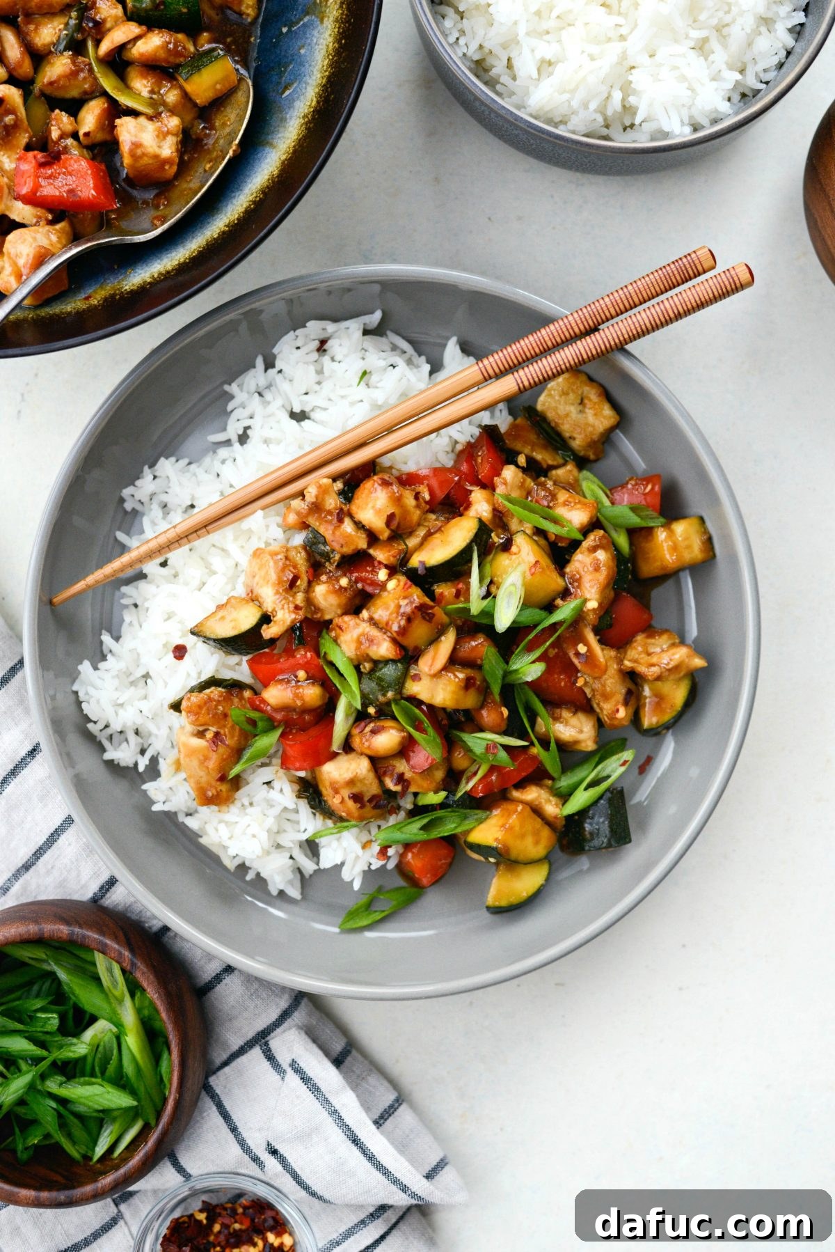 A close-up shot of the finished Kung Pao Chicken Stir-fry in a grey bowl, highlighting the tender chicken, vibrant vegetables, and rich sauce, with chopsticks resting on the side.