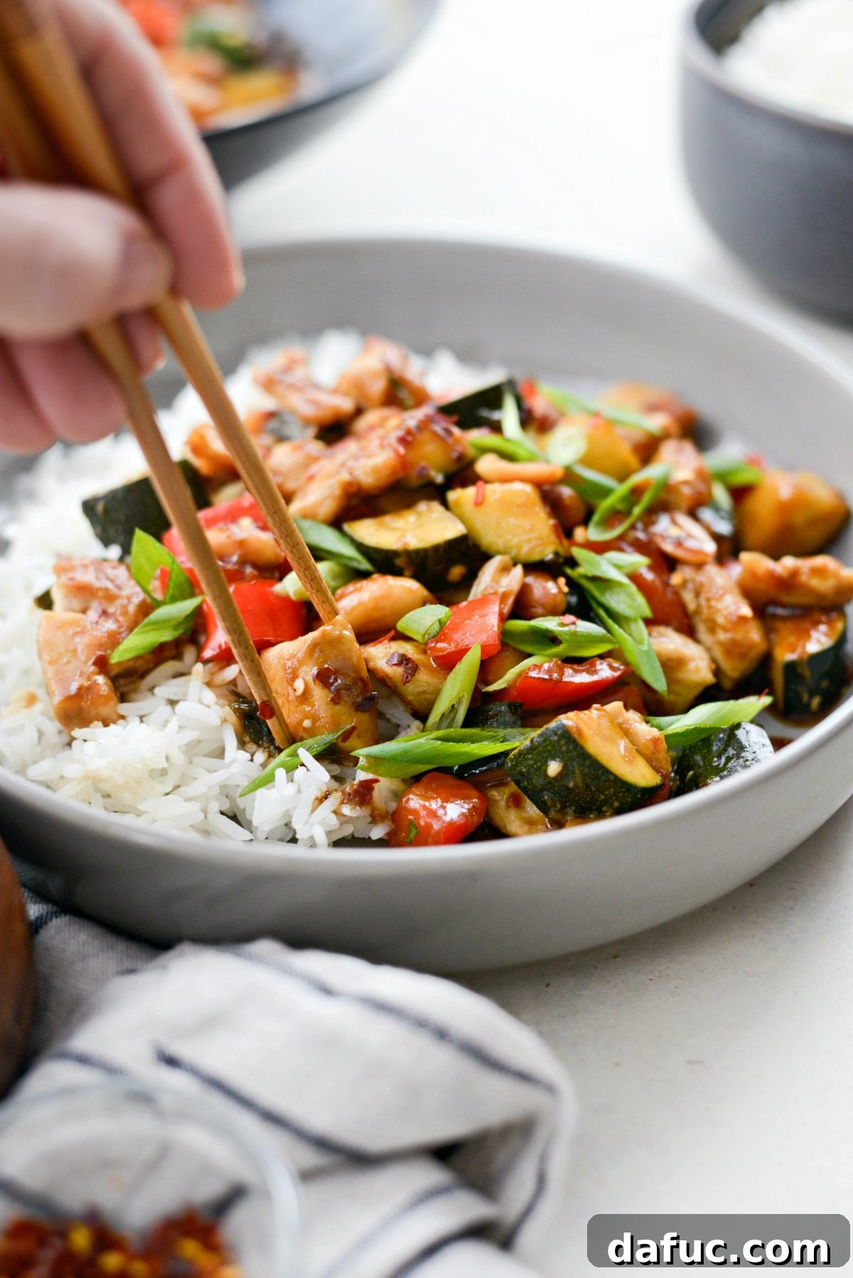 A close-up image showing a piece of Kung Pao Chicken being picked up with chopsticks, ready to be enjoyed.