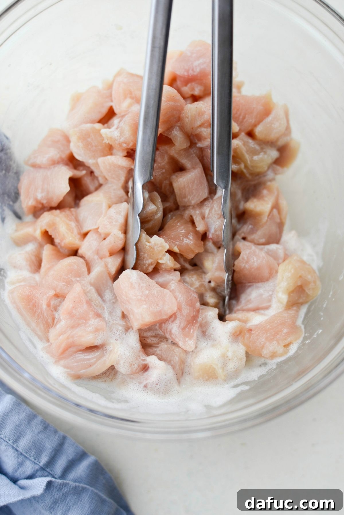 Close-up of chicken pieces, now fully coated in the egg white mixture, ready for cooking, highlighting the uniform and slightly textured surface.