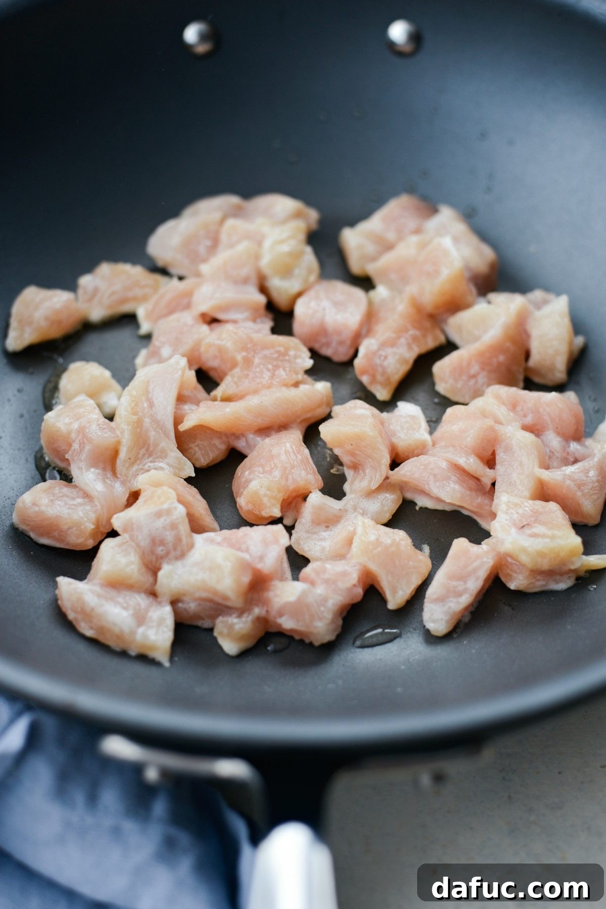 Coated chicken pieces beginning to sear in a very hot wok with peanut oil, showing the initial stages of browning and crisping.