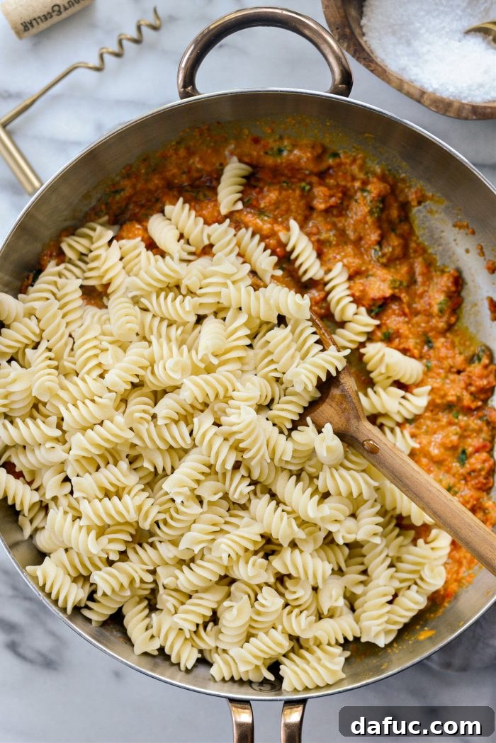 Golden Walnut & Sun-dried Tomato Pesto Pasta 13 Cooked pasta and reserved pasta water being added to the sun-dried tomato pesto sauce in the skillet