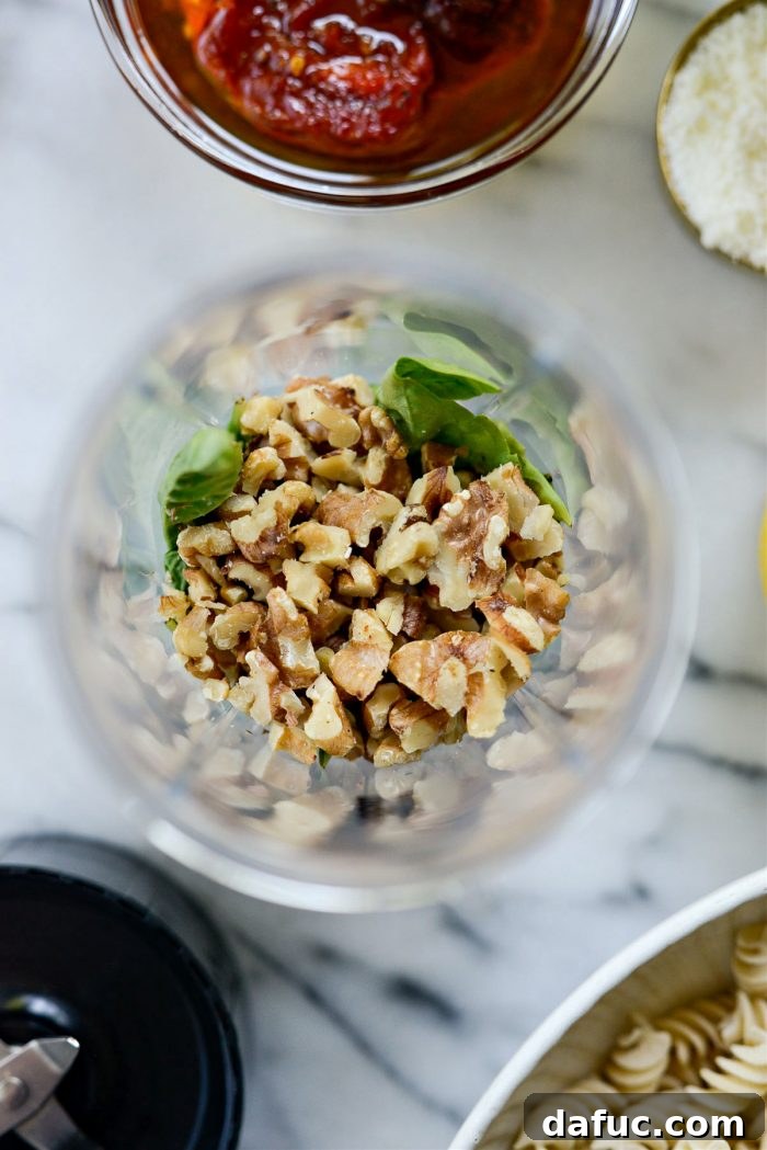 Golden Walnut & Sun-dried Tomato Pesto Pasta 7 Roughly chopped toasted walnuts being added to the blender with basil