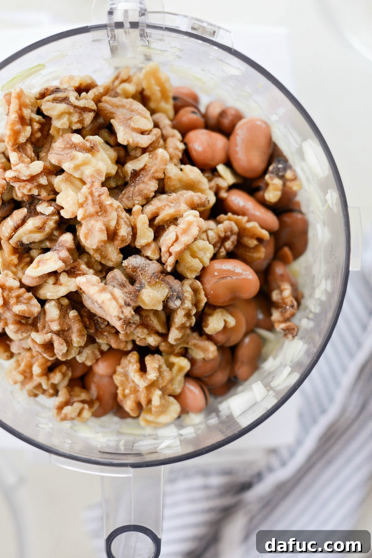 Fava beans and walnuts added to a food processor with onion and garlic