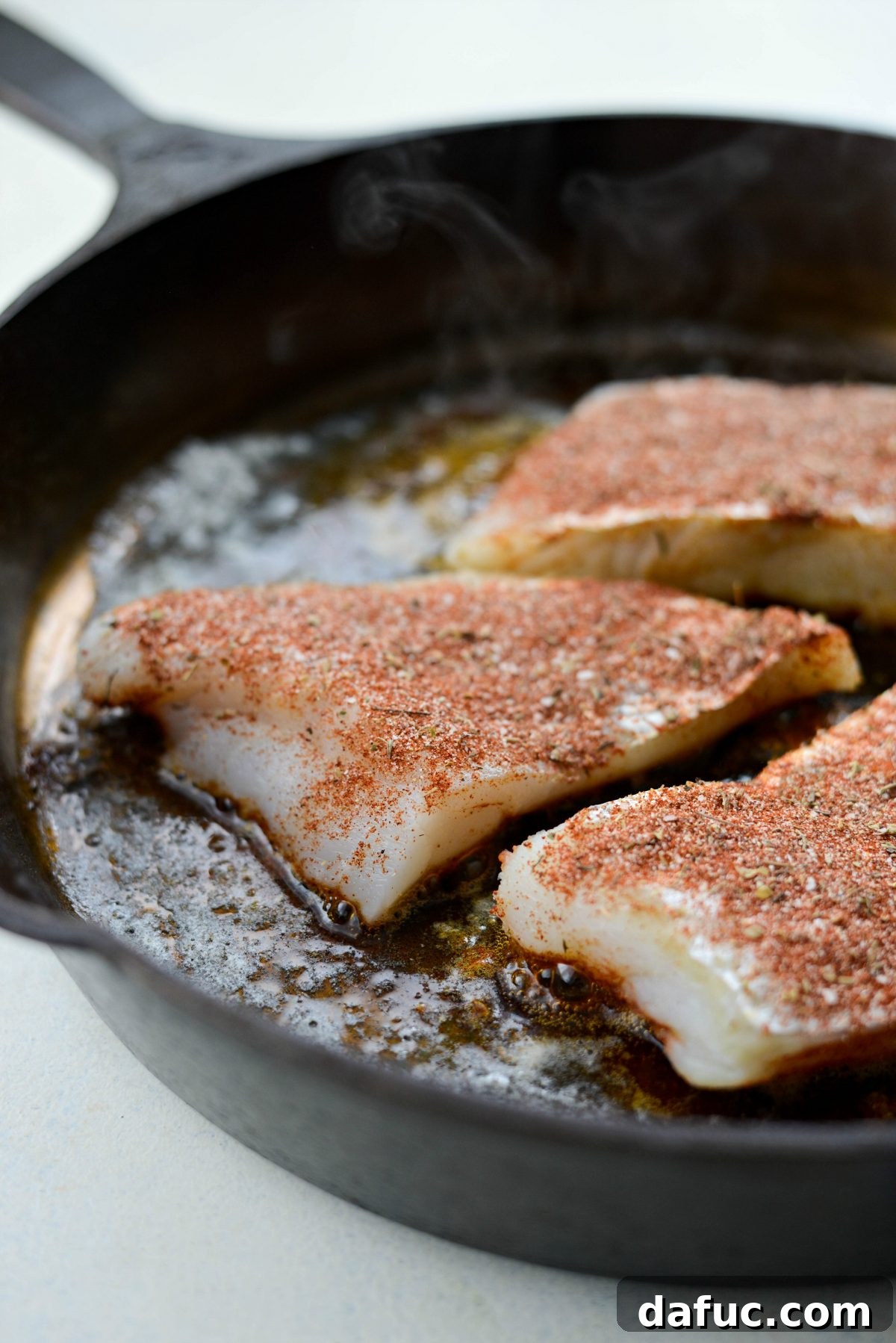 Blackened fish cooking on both sides in a hot skillet