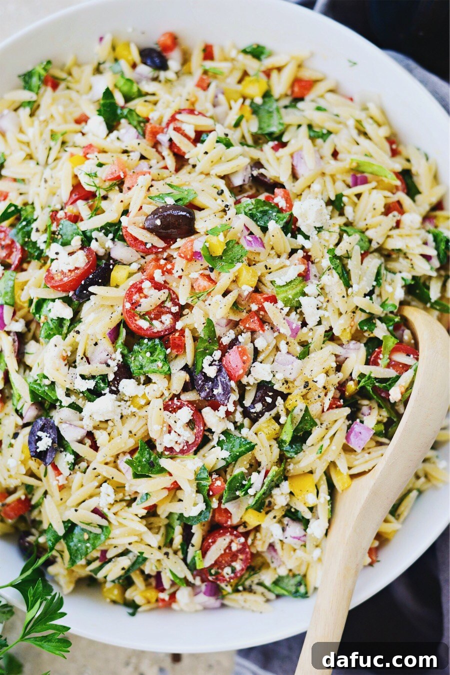 Vibrant Mediterranean Orzo Salad 11 Greek Orzo Salad served in a white bowl with a wooden spoon