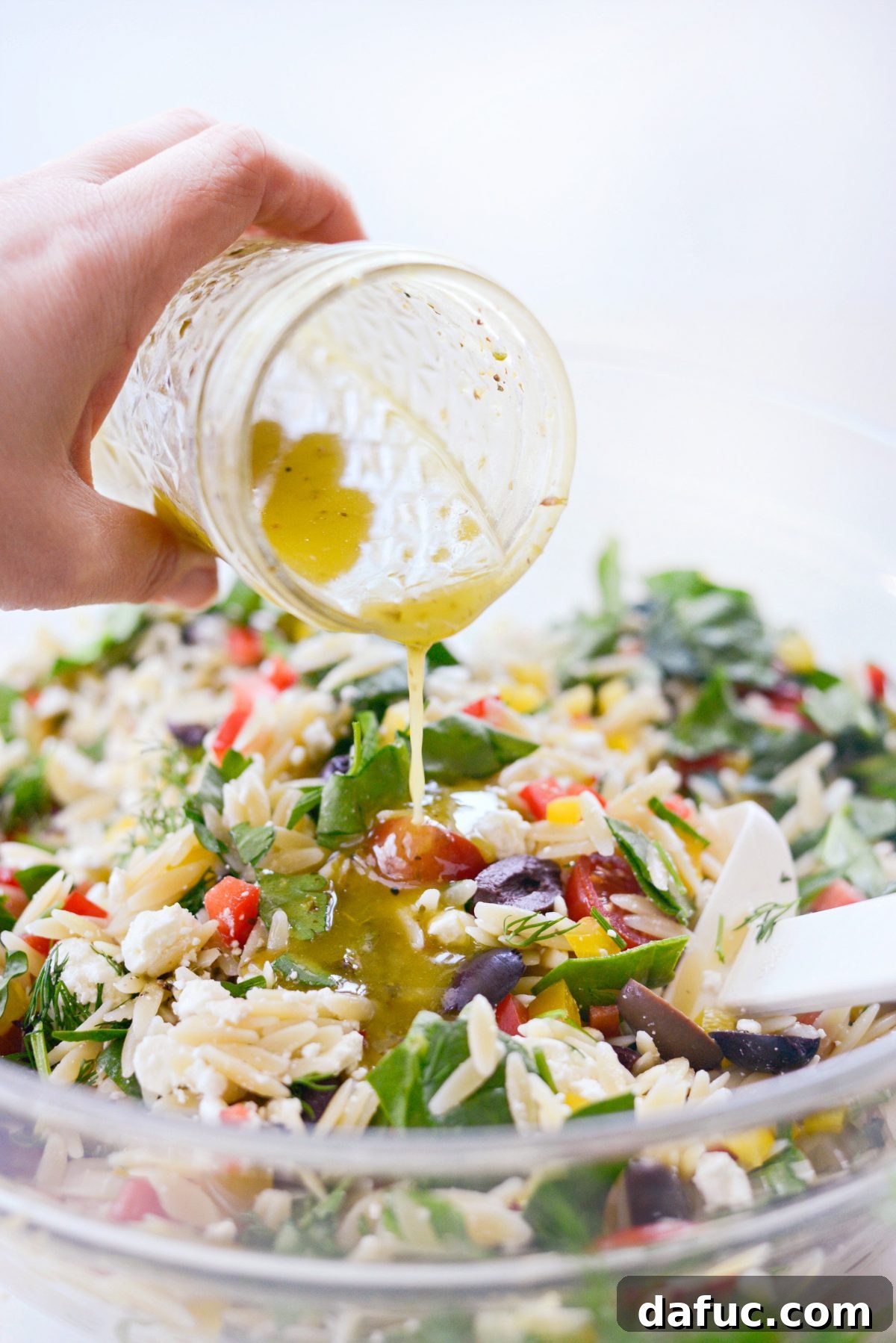 Vibrant Mediterranean Orzo Salad 9 Pouring homemade Greek Salad Dressing onto the mixed salad