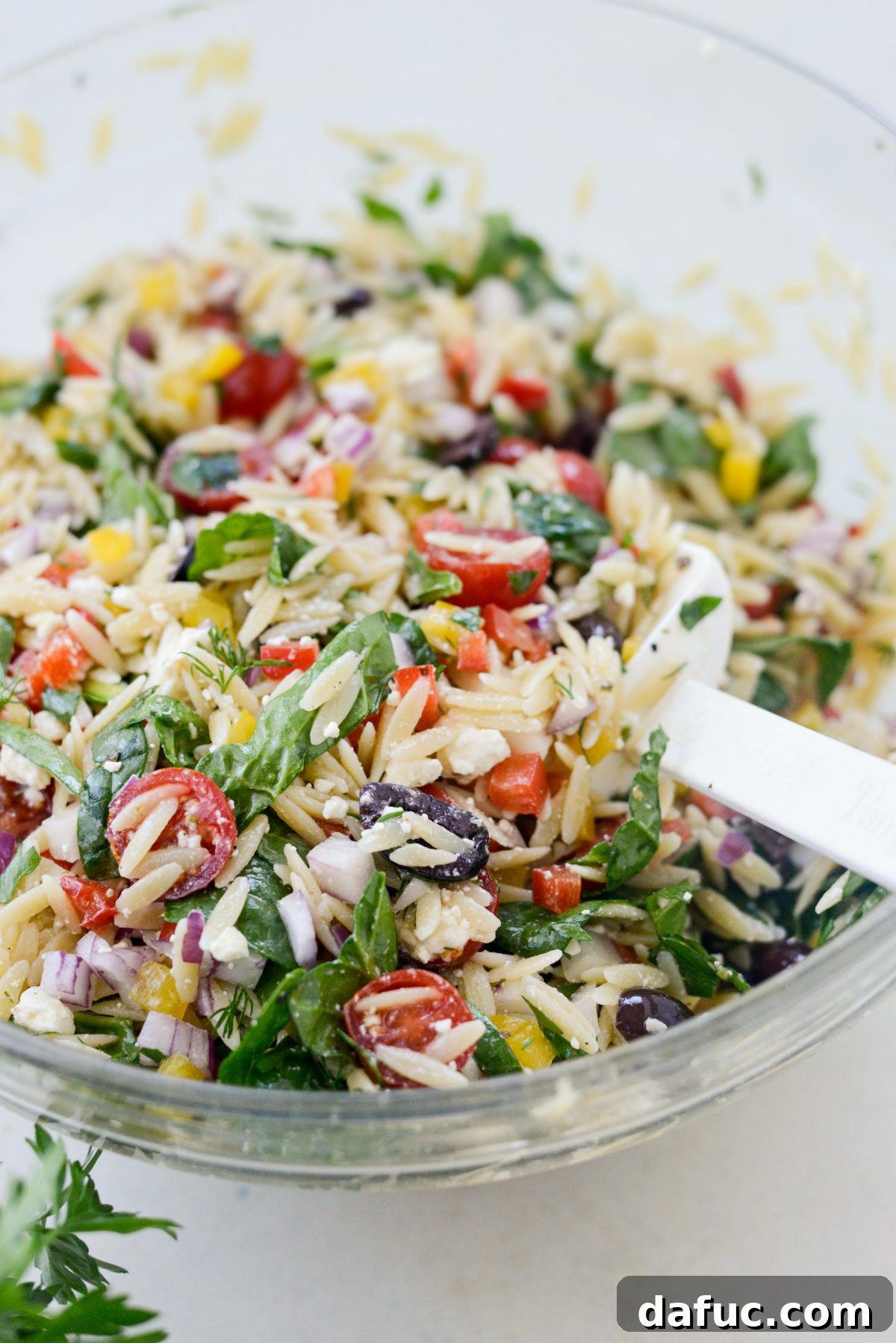 Vibrant Mediterranean Orzo Salad 10 Tossing the Greek Orzo Salad with a white rubber spatula in a bowl