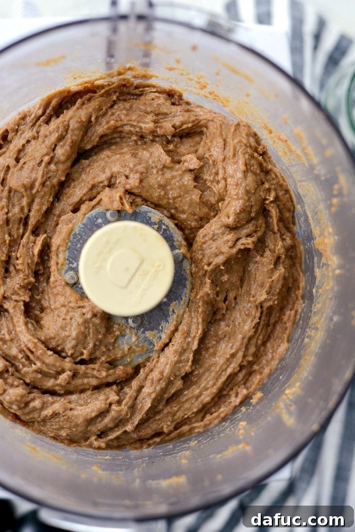 Craft Your Own Speculoos Cookie Butter 10 A rubber spatula scraping down the sides of the food processor bowl, ensuring all ingredients are mixed into the cookie butter.