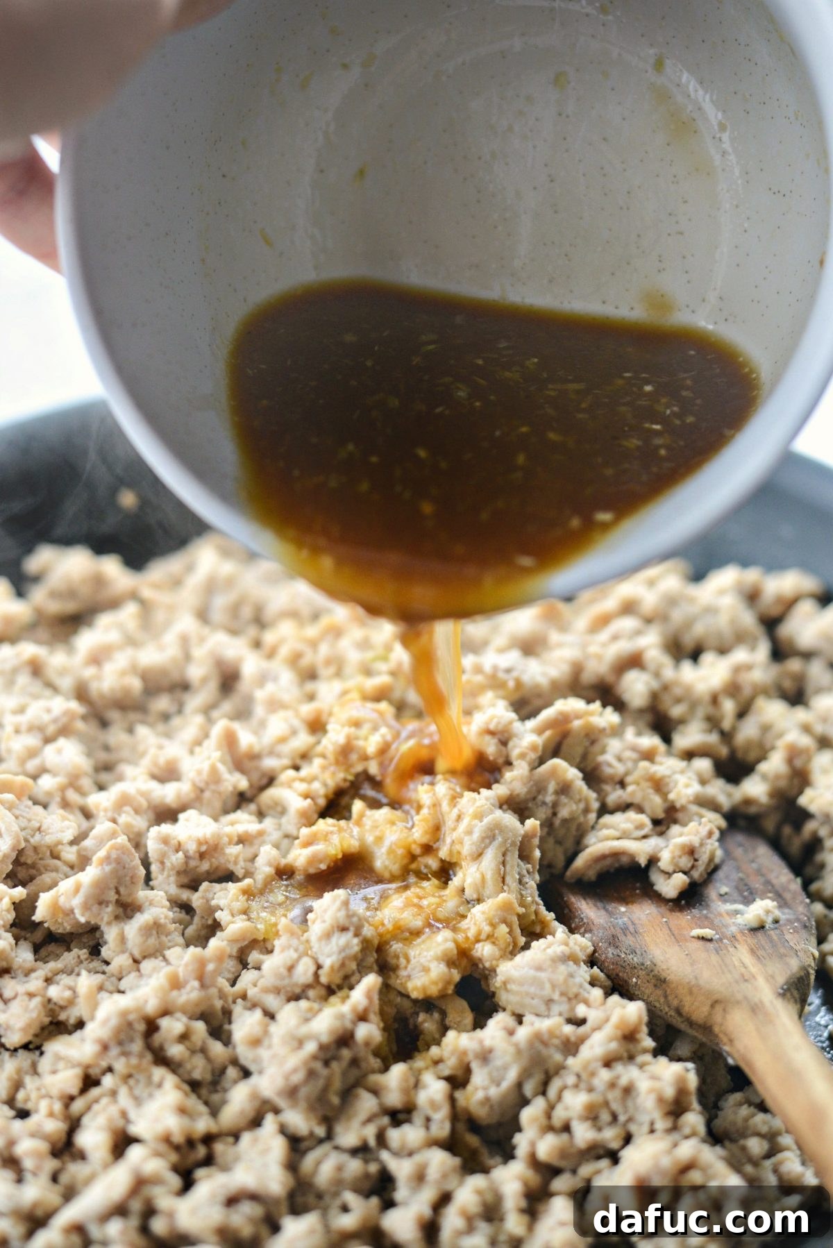 Pouring the aromatic Thai sauce over cooked ground chicken in a skillet