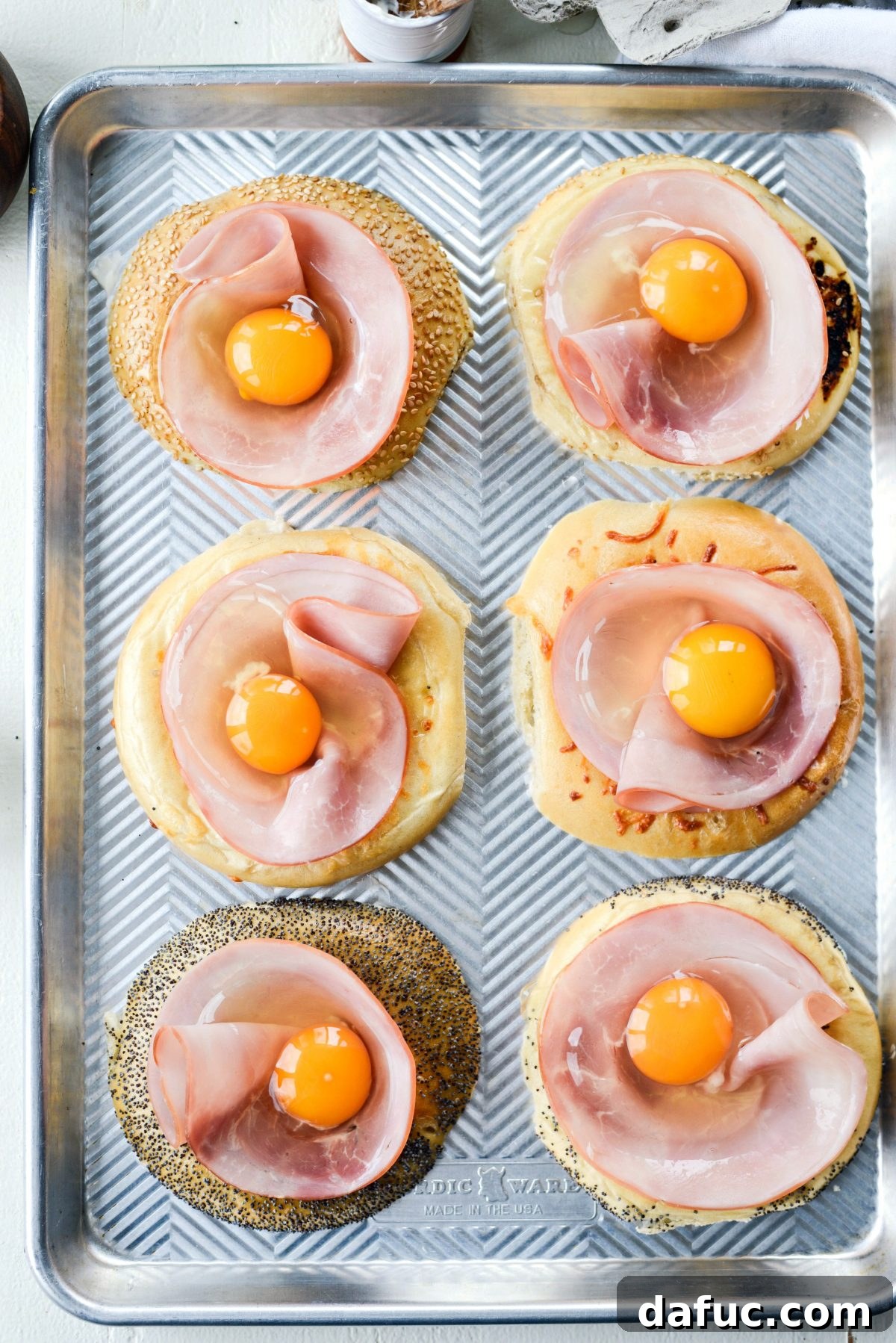 Bagel Egg Nests 11 A hand placing a slice of ham and cracking an egg into a bagel hole