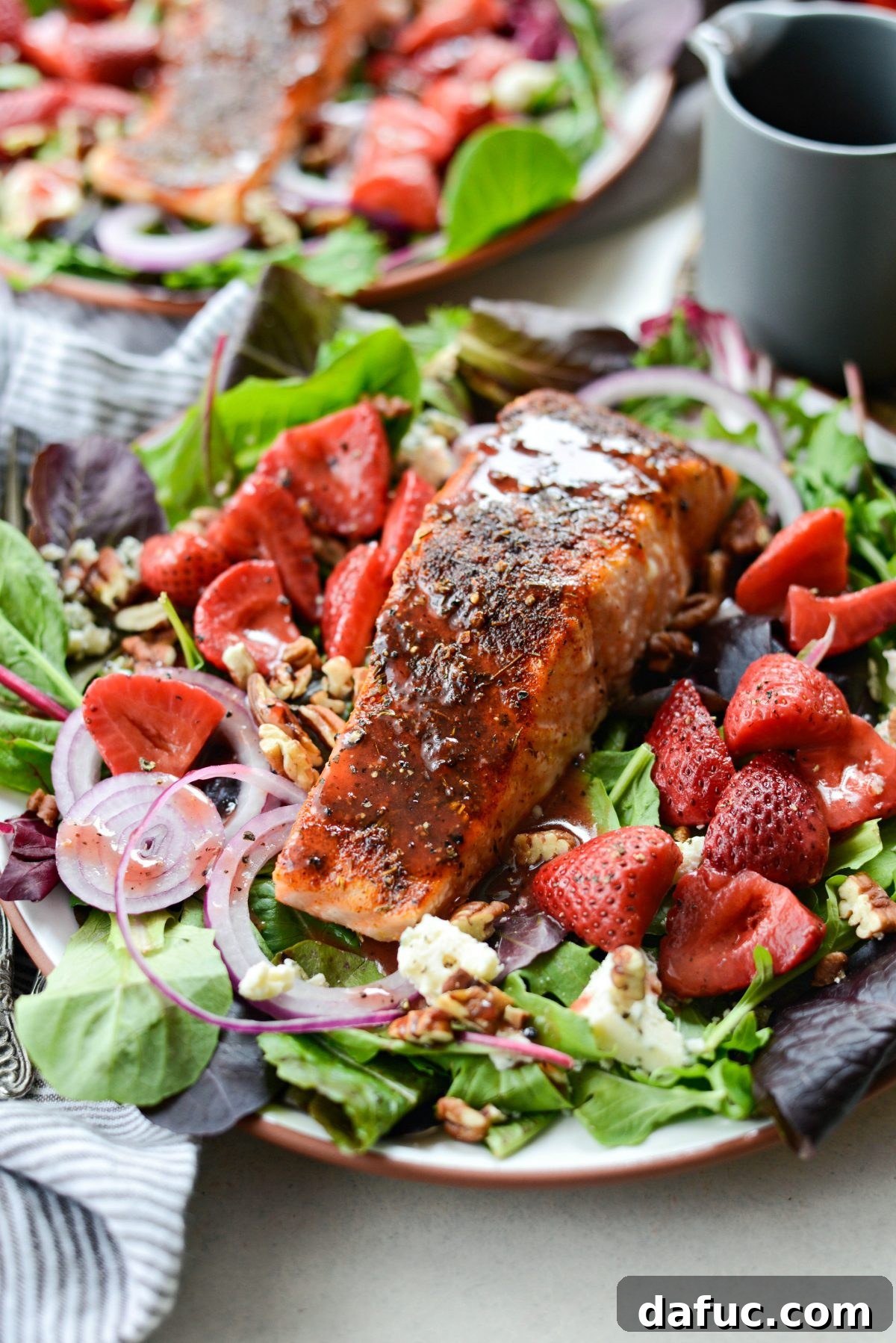 Close-up of a beautifully arranged Blackened Salmon Salad with vibrant spring greens, red onion, blue cheese, pecans, and pickled strawberries.