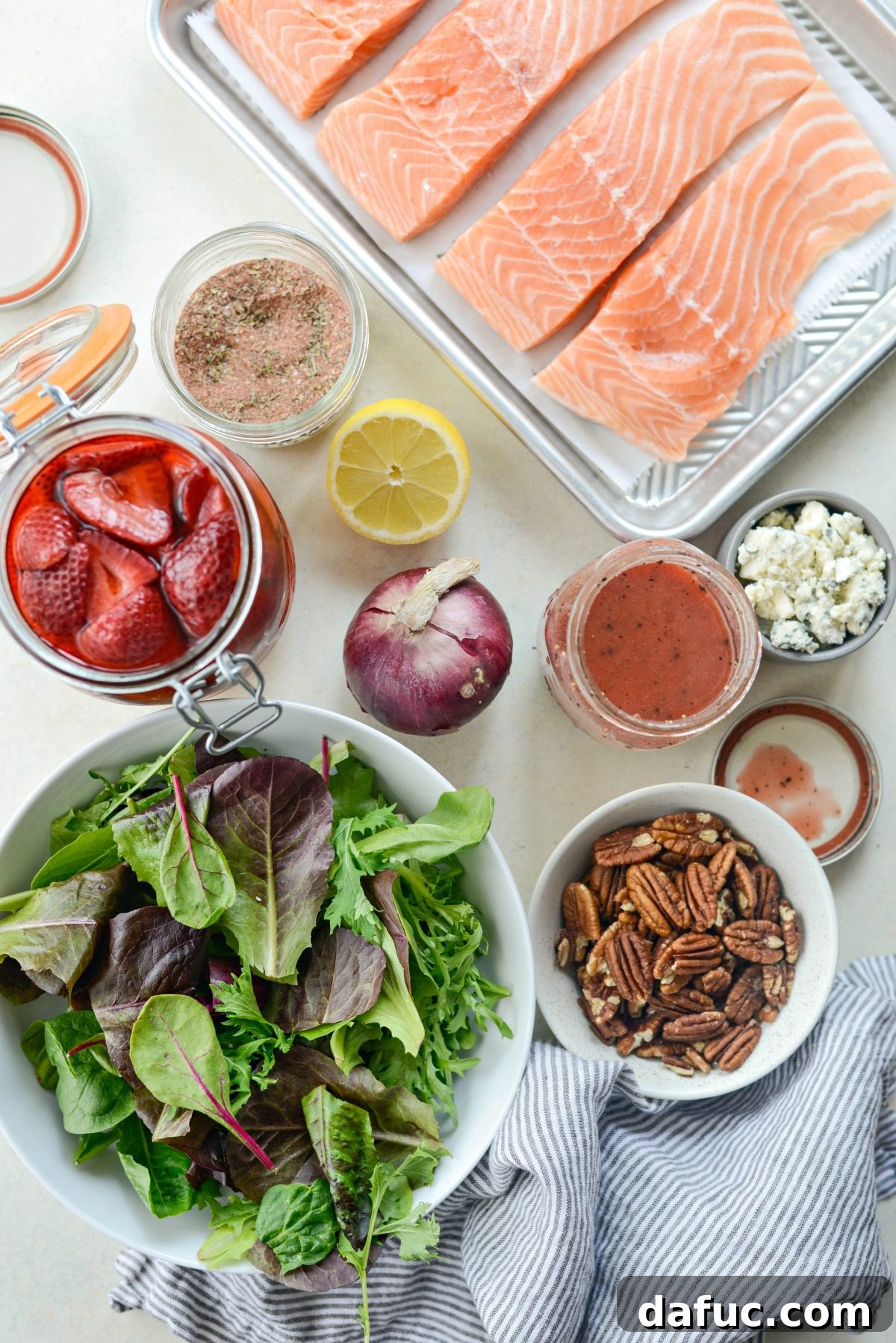 Ingredients laid out for Blackened Salmon Salad, including salmon fillets, seasoning, spring greens, and vinaigrette components.