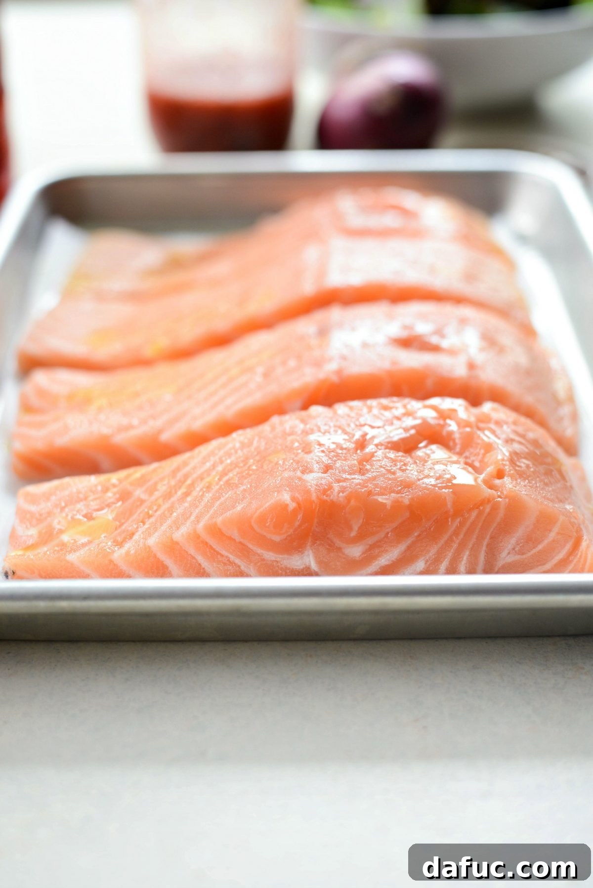 Four raw salmon fillets seasoned with blackened spices, ready for baking.