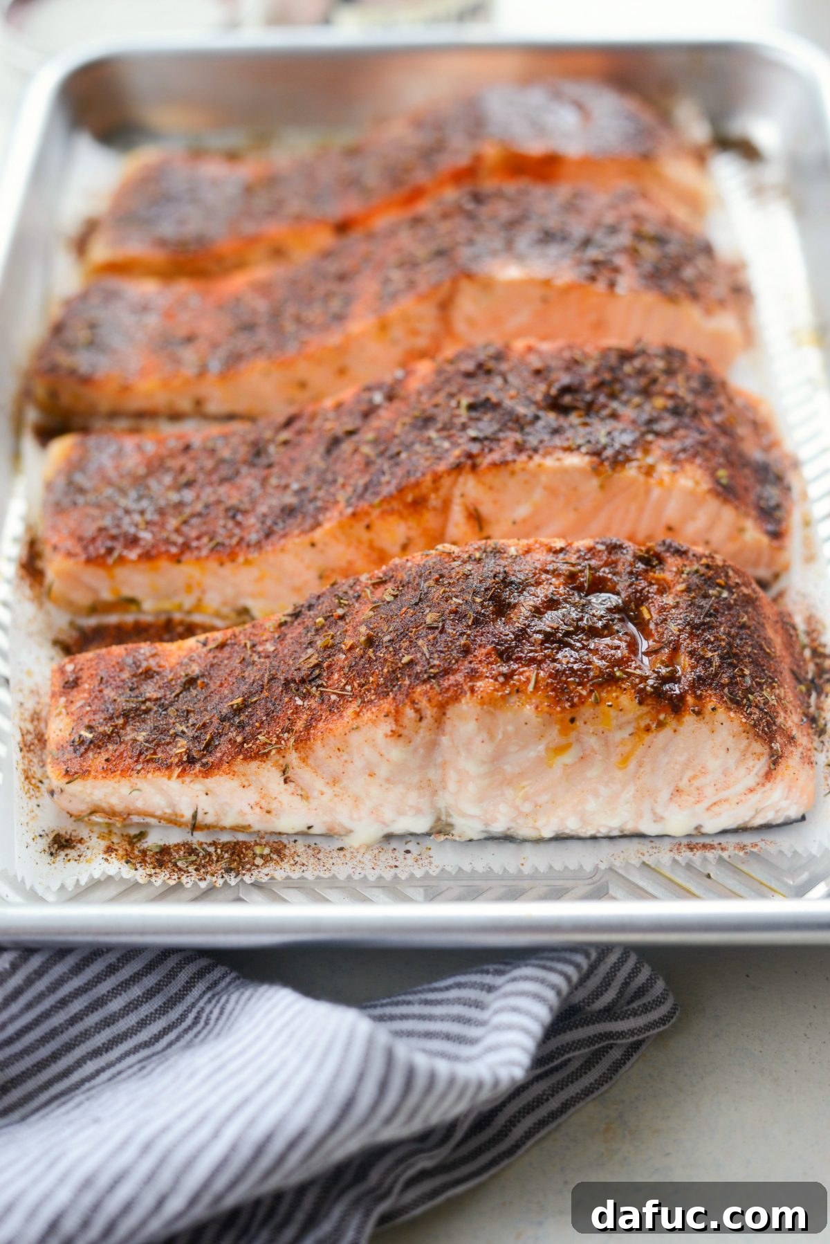 Cooked blackened salmon fillets cooling on a baking sheet, showcasing their dark, seasoned crust.