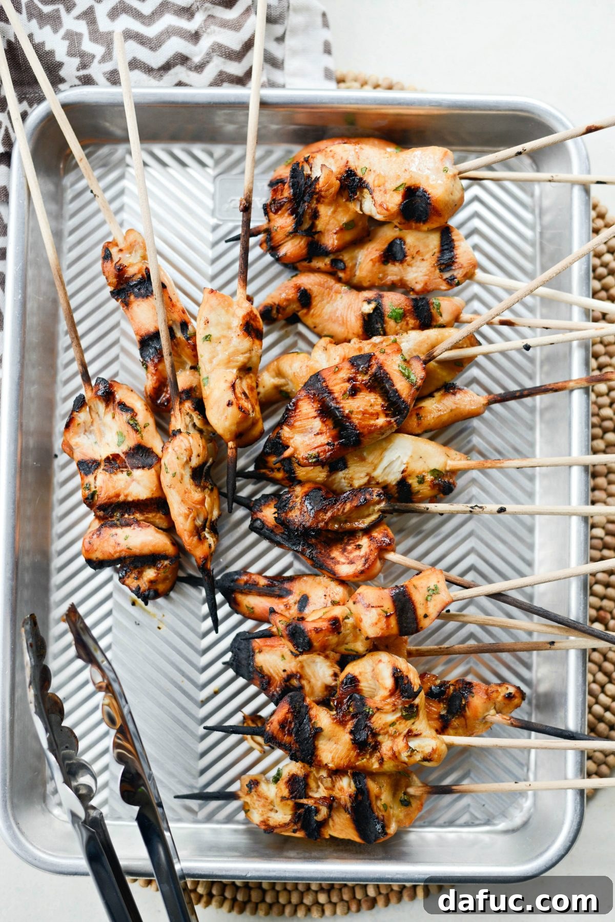 Thai Chicken Satay Skewers with Creamy Peanut Sauce 14 Beautifully grilled Thai chicken skewers resting on a pan