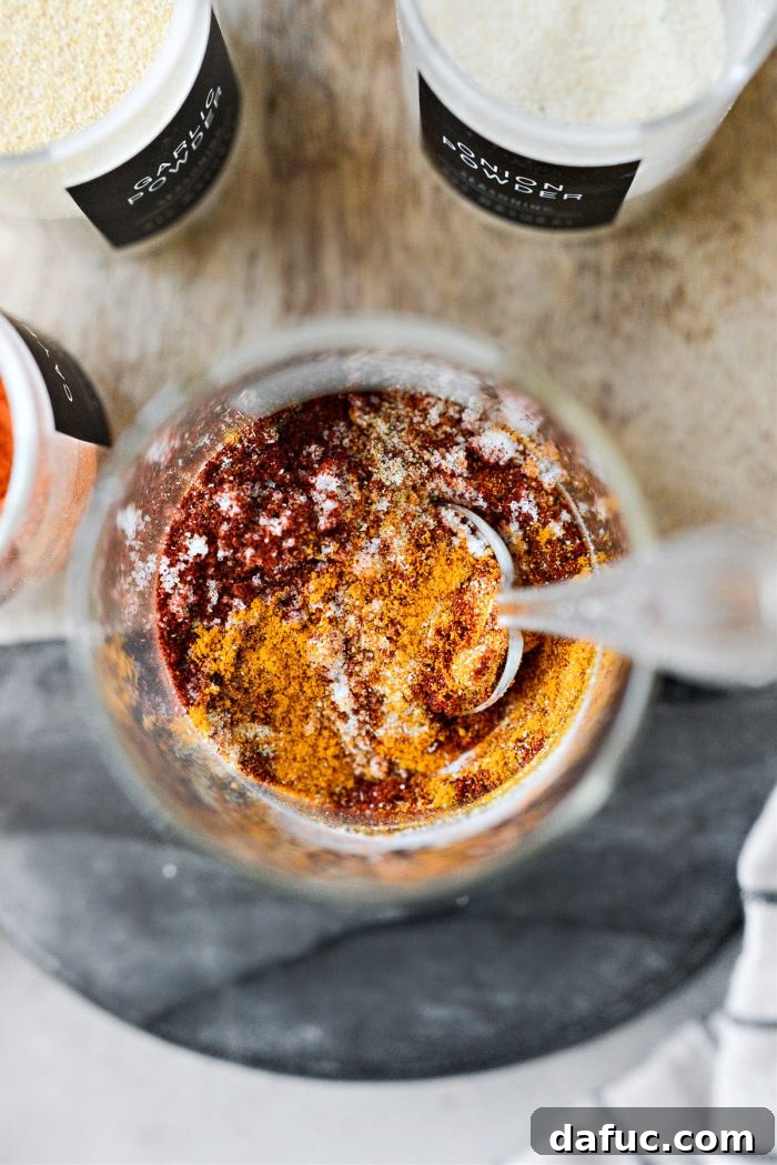 A small whisk stirring the measured spices in a glass jar