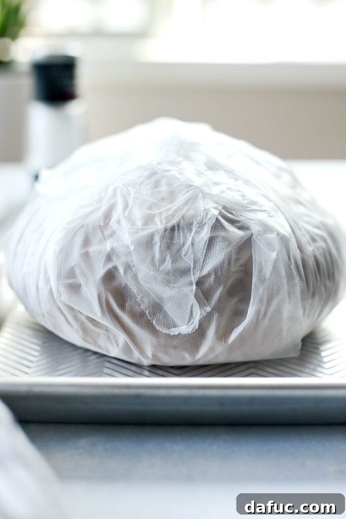The California Club Loaf Sandwich wrapped tightly in plastic wrap, ready for chilling.