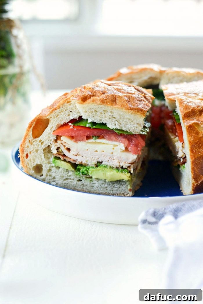 Golden State Club Loaf 3 Inside view of the California Club Loaf Sandwich, showcasing vibrant layers of avocado, bacon, deli meat, cheese, tomato, and basil.