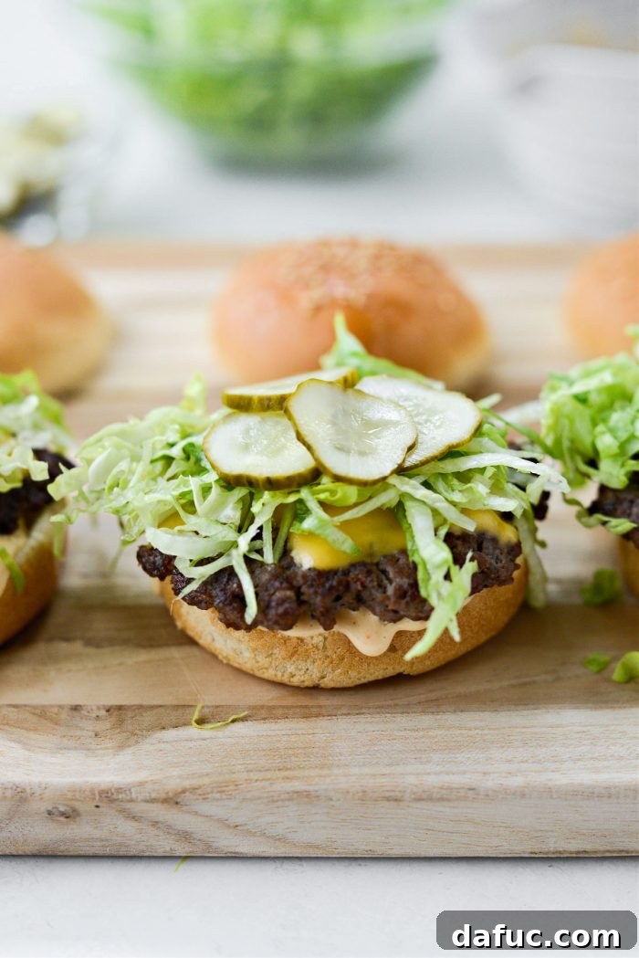 Mac Mini Bites 17 Layering a slider bun with a burger patty, shredded lettuce, and pickle slices.
