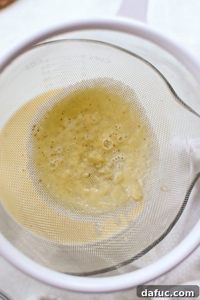 Golden Brown Butter Indulgence 15 Straining the thickened ice cream base through a mesh strainer into a large bowl.
