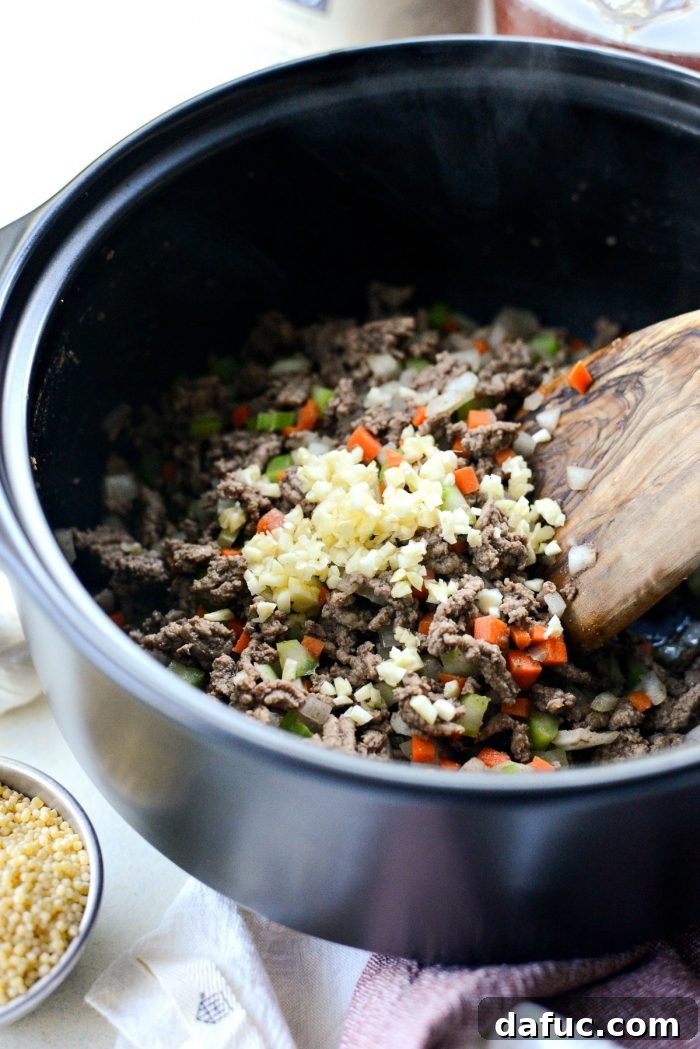 Diced carrots, celery, and onion sautéing with browned ground beef in a Dutch oven, forming the aromatic base of the soup.
