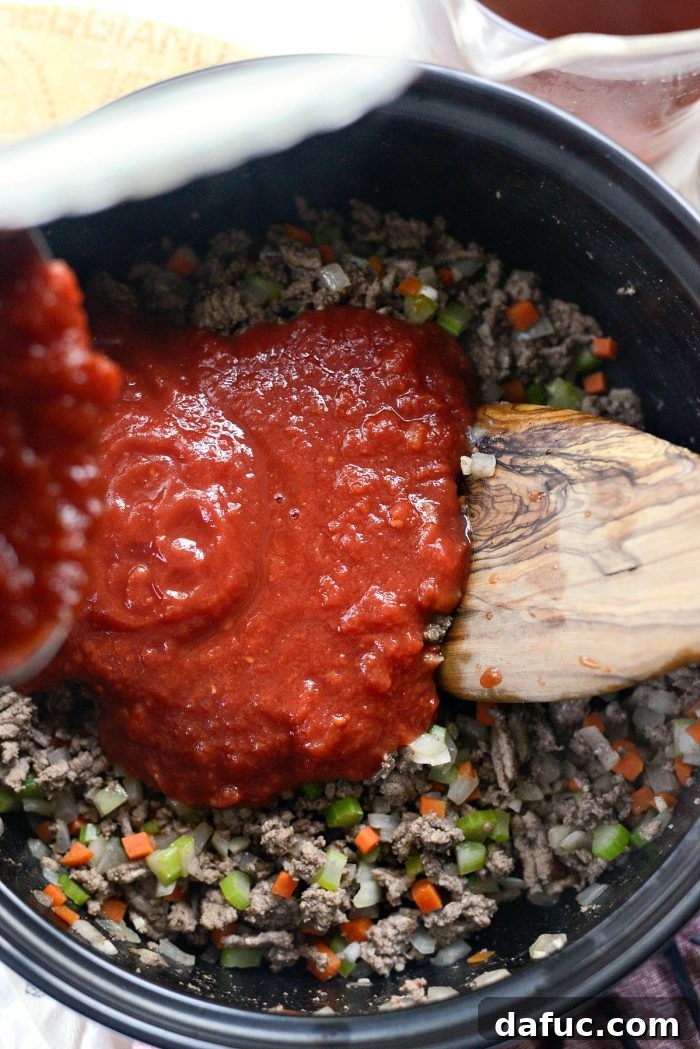 Minced fresh garlic being added to sautéed ground beef and vegetables in a Dutch oven.