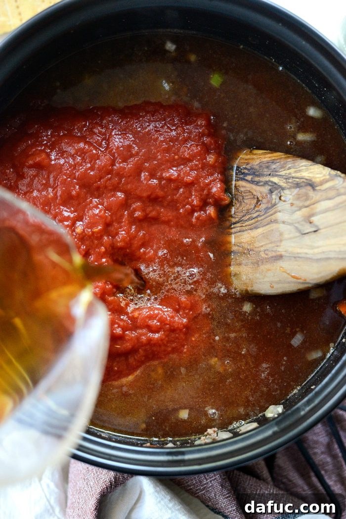 A 28-ounce can of crushed tomatoes and beef stock being poured into the Dutch oven with the sautéed beef and vegetables.