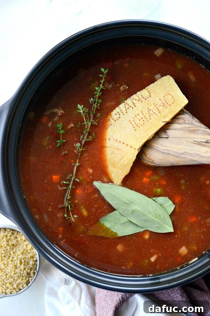 Bay leaves, fresh thyme sprigs, and a parmesan rind added to the simmering tomato beef broth in a Dutch oven.
