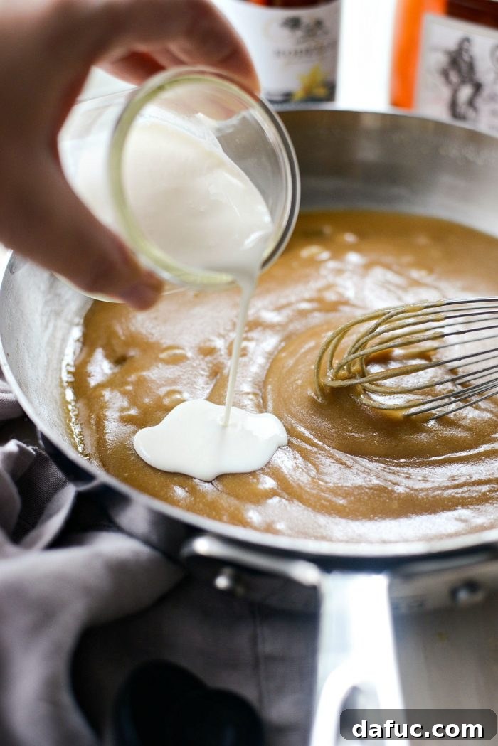 Pouring heavy whipping cream into the butter and sugar mixture, whisking to combine for the butter rum sauce.