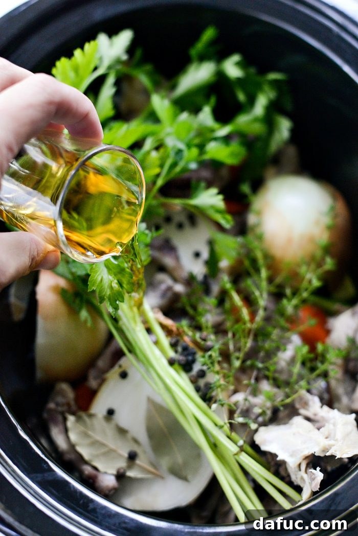 Low & Slow Chicken Broth 8 Pouring apple cider vinegar into a slow cooker with chicken bones and vegetables, demonstrating a key step for mineral extraction. #applecidervinegar #stocksecrets #nutrientextraction
