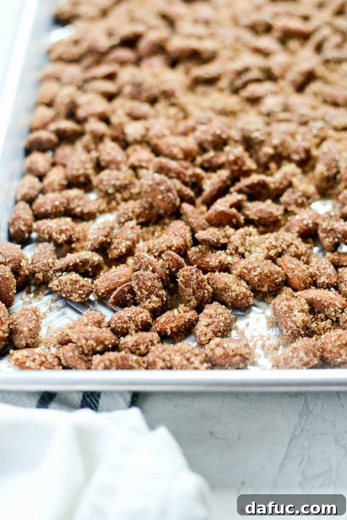 Irresistible Cinnamon Sugar Almonds 11 Cinnamon sugar almonds spread in a single layer on a parchment-lined baking sheet, ready for baking.