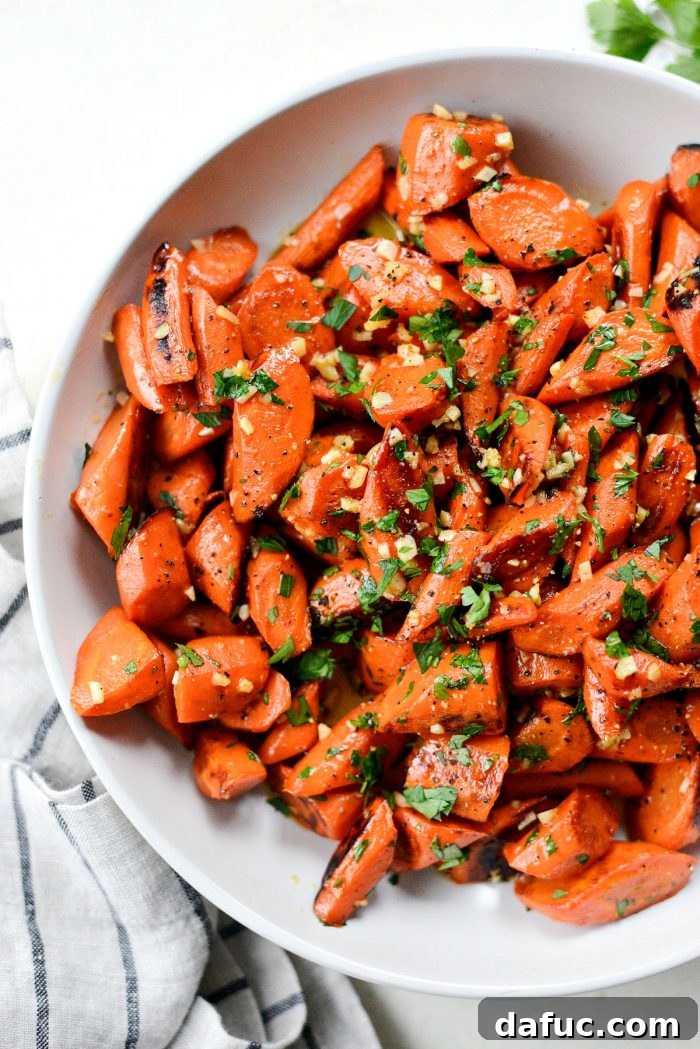 A serving of garlic butter roasted carrots on a plate, topped with a generous amount of freshly ground black pepper.