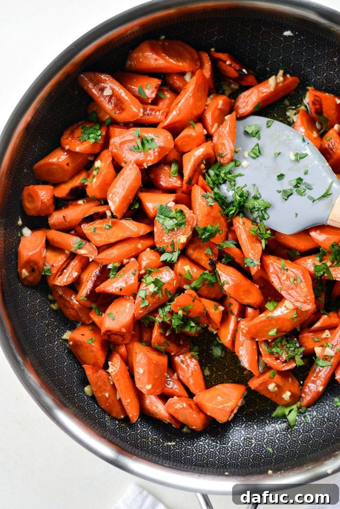 Roasted carrots being tossed in the skillet with melted garlic butter, ensuring every piece is coated.
