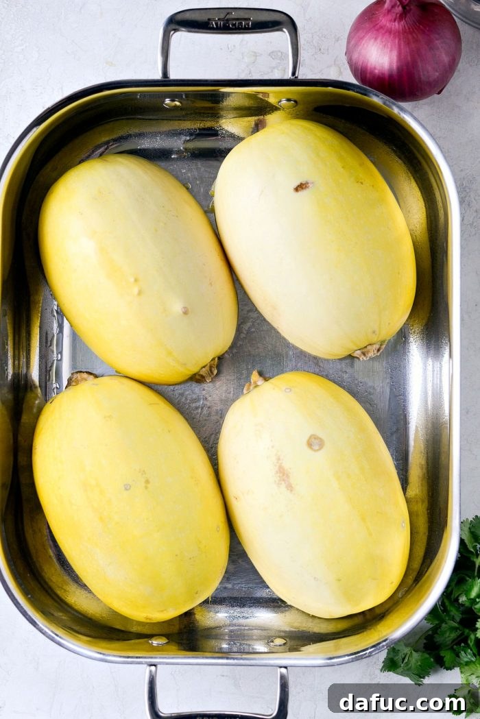 Raw spaghetti squash halves on a baking sheet, ready for roasting. A crucial step for the stuffed squash recipe.