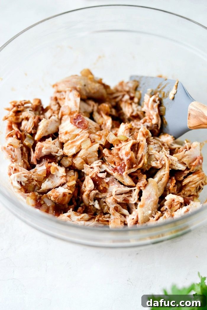 The chicken, bacon, onion, garlic, and BBQ sauce mixture being stirred thoroughly in a bowl, ready to stuff the spaghetti squash.