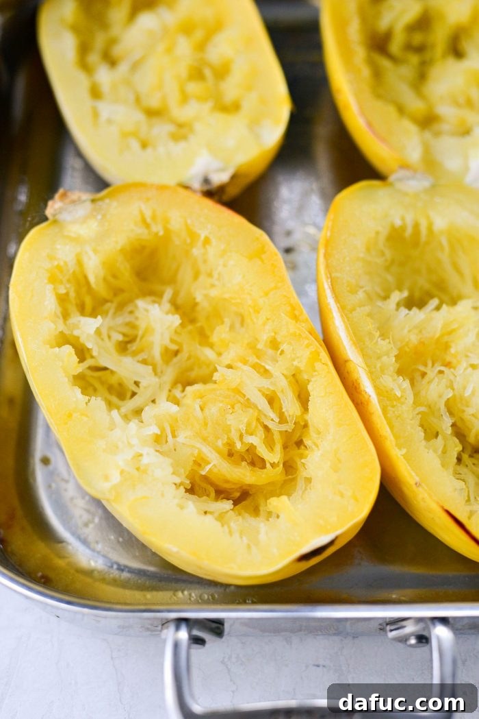 Spaghetti squash strands being scraped from the roasted squash halves using a fork, showing the pasta-like texture.